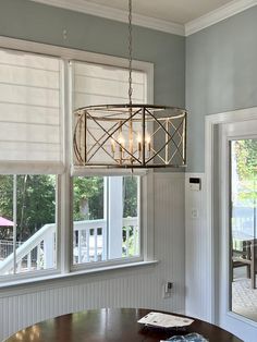 a light fixture hanging from the ceiling over a table in a room with white walls and windows