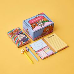 an open box with some writing supplies on it and a notepad next to it