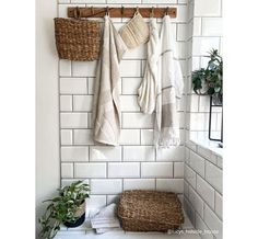 towels are hanging on the wall next to a basket and potted plant in a white tiled bathroom