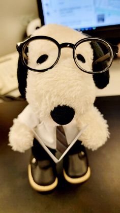 a stuffed dog with glasses and a tie sitting in front of a laptop computer on a desk