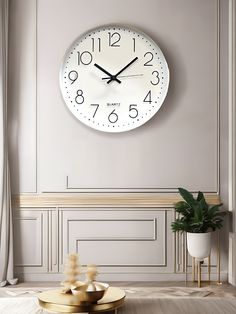 a large white clock mounted to the side of a wall next to a table and potted plant