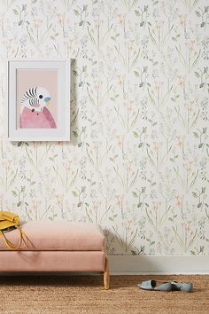 a pink bench sitting in front of a wall with flowers on it and a painting hanging above