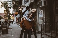 two young women are hugging on the sidewalk