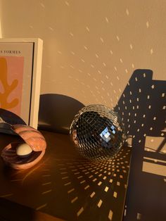 a mirror ball sitting on top of a wooden table next to a book and chair