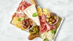 an assortment of meats and cheeses on a white platter with olives