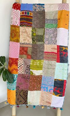 a multicolored patchwork blanket sitting on top of a wooden chair next to a potted plant