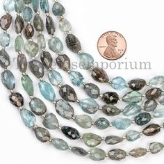 a long necklace with many faceted blue and green stones on it, next to a penny