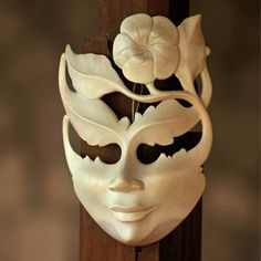 a white mask with flowers on it hanging from the side of a wooden pole in front of a wall