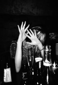 a woman sitting at a table with her hands in the air and two empty wine glasses next to her