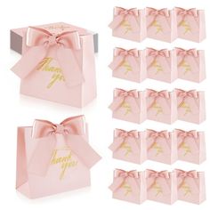 twelve pink gift bags with gold foil lettering and bows on the front, each in different sizes