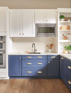 a kitchen with white cabinets and blue drawers, an oven in the corner and a microwave on the wall