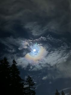 the moon is shining brightly in the cloudy sky above some pine trees and evergreens