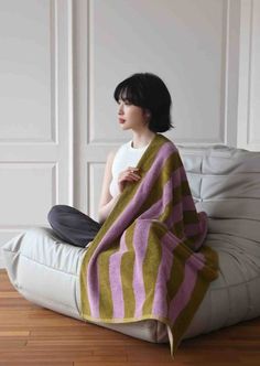 a woman sitting on top of a white couch covered in a purple and yellow striped blanket