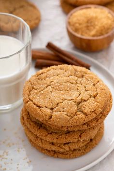 three cookies on a white plate next to a glass of milk and cinnamon sticks in the background