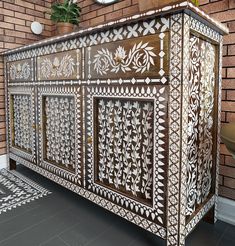 an ornately decorated sideboard in front of a brick wall with a clock on it