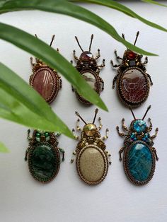 six insect brooches sitting on top of a white surface next to a green plant