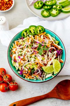 a colorful salad in a bowl with limes, tomatoes and peppers on the side