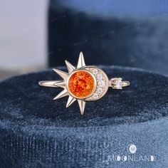 a ring with an orange stone in the center on a blue velvet cushioned surface