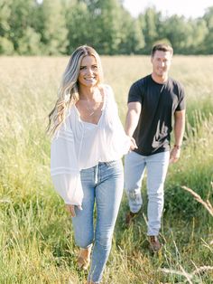 a man and woman are walking through the tall grass with trees in the back ground