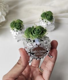 a person holding a small silver box with succulents in it and two smaller green flowers on top