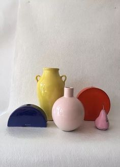 three different colored vases sitting next to each other on a white surface with one pink, one blue and one yellow