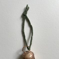 a necklace with a bell hanging from it's side on a string that is attached to a wall