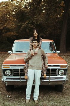 a man standing next to a woman on the back of an orange truck in front of trees