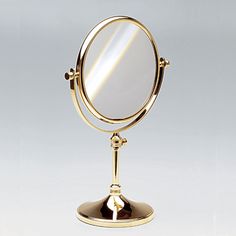 a gold colored mirror on a stand against a white background with the reflection of it's own image