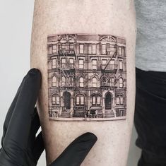 a person with a tattoo on their arm holding up a black and white drawing of a building