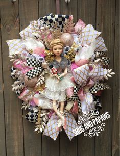 a wreath with a doll on it hanging from the side of a wooden fence next to a wall