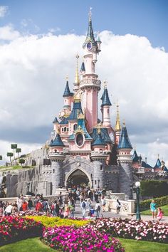 the castle is pink and blue with many people walking around it in front of flowers