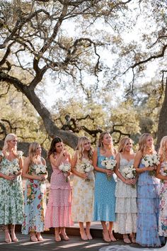 a group of women standing next to each other in front of a tree holding bouquets