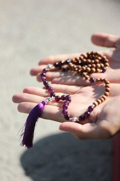 this 108 bead mala is designed by here & there creative and handmade in northern india with sandalwood and lava stone beads. the beads originate from the spiritual lands of northern india and have been blessed by the holy ganges river.  amethyst, a favorite stone for many, is known to assist with problem-solving and making clear, articulate decisions. here & there styling tip: if the tassel strands become tangled, dip in a cup of water and hang to let dry. materials: natural sandalwood and ameth Spiritual Mala With 8mm Beads For Healing, Spiritual Brown Mala For Healing, Holistic Mala With 8mm Beads For Festivals, Holistic Mala With 108 Beads For Healing, Spiritual Wooden Beads Mala For Festival, Holistic Mala With 108 Beads For Festival, Dip In A Cup, Spiritual Mala With 108 Beads For Festival, Spiritual Brown Mala For Meditation