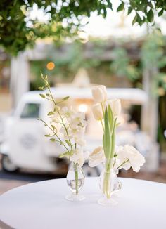 two vases filled with flowers sitting on top of a white tablecloth covered table