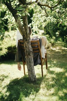 a woman sitting in a chair under a tree with her back turned to the camera