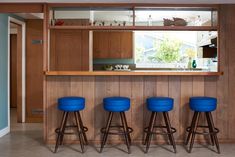 three blue stools sit in front of a wooden bar with built - in shelves