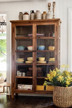 a wooden cabinet with glass doors and shelves filled with plates, bowls and other items