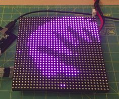 an electronic device with purple lights on it and wires attached to the board, sitting on top of a green cutting mat