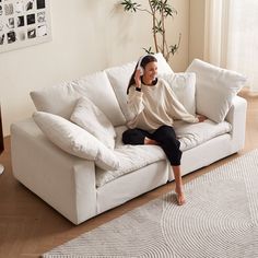 a woman sitting on top of a white couch talking on a cell phone while wearing black pants