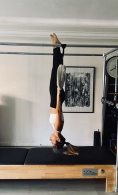 a woman doing a handstand on top of a black mat in a room