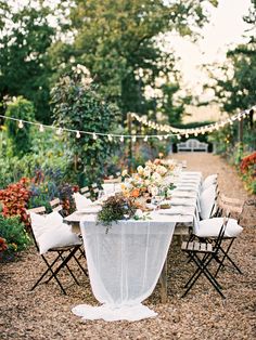 an outdoor table set up with white linens and flowers on it for a dinner party