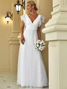 a woman in a white wedding dress standing next to a wall and holding a bouquet