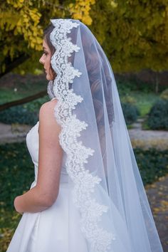 a woman wearing a wedding veil in front of trees and bushes with yellow flowers on it