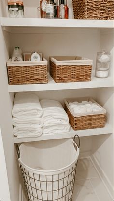 an organized bathroom closet with baskets and towels