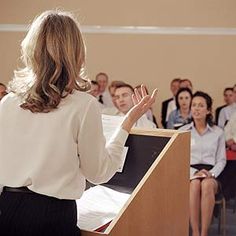 a woman standing at a podium in front of an audience with her hands up to the side