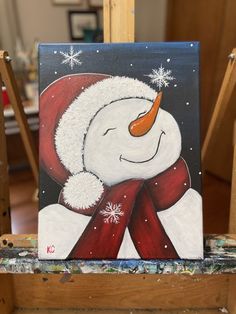 a painting of a snowman wearing a red hat and scarf on a easel