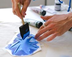 two hands are working on an origami snowflake with paint and glue