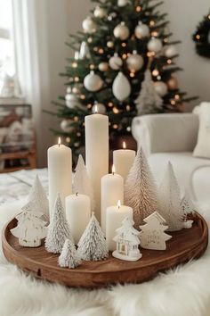 white candles are arranged on a wooden tray in front of a christmas tree and other decorations