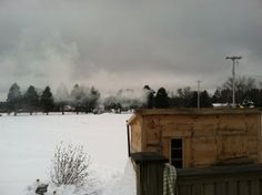 a snow covered field with a building in the distance and trees on top of it