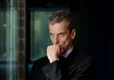 a man in a suit and tie leaning against a wall with his hand on his chin